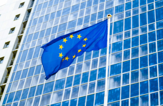 Image of EU flag fluttering on wind against high business office building made of concerete and glass. Concept of ecenomics, development, government and politics